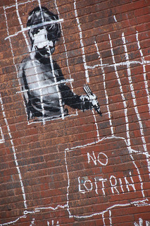 Stencil art on a wall showing a boy scrawling 'No loitrin'
