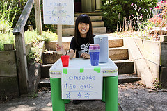 A girl promotes her lemonade stand with handwritten signs.