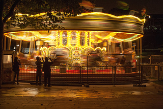 Night time: Fairground carousel speeds around as passers-by watch.